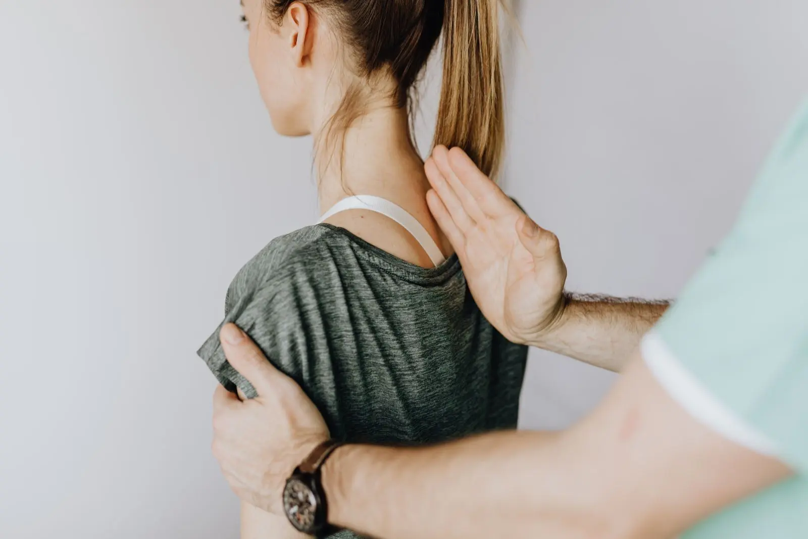Les mains d'un physiothérapeute qui examinent l'épaule et la nuque d'une patiente.